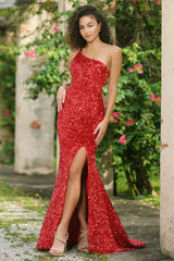 Woman in a red one-shoulder dress standing outdoors with greenery and flowers in the background