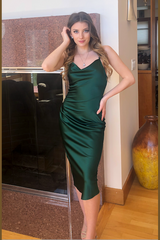 Woman in a green dress standing in a room with a large mirror and decorative vase.
