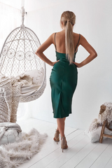 Woman in a green dress standing in a room with a white chair and decor.
