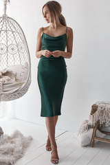 Woman wearing a green dress standing in a minimalistic room with a white wall and wooden floor.