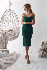 Woman in a green dress standing in a room with a white chair and decorative items.