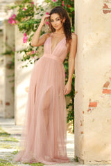 Woman in a pink dress standing against a stone wall with greenery in the background