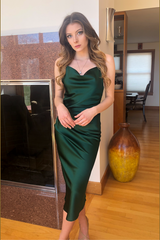 Woman in a green dress standing in a room with wooden floor and large mirror.