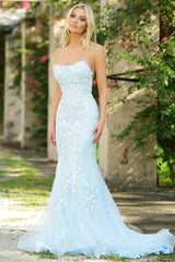 Woman in a light blue evening gown standing outdoors with greenery in the background