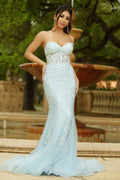 Woman in a light blue strapless gown standing outdoors with greenery in the background