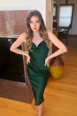 Woman in a green dress posing in a room with wooden floor and decorative items.