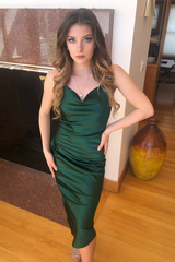 Woman in a green dress standing indoors with a vase and wall art in the background