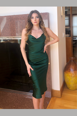 Woman wearing a green dress standing indoors next to a fireplace.